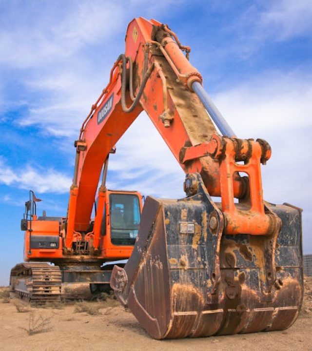 A large orange excavator working on a construction site under a blue sky.